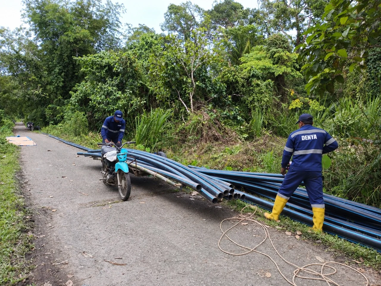 Pipa HDPE hitam bergaris biru dan tim berseragam DENYA di jalan lokasi Leubang Hulu